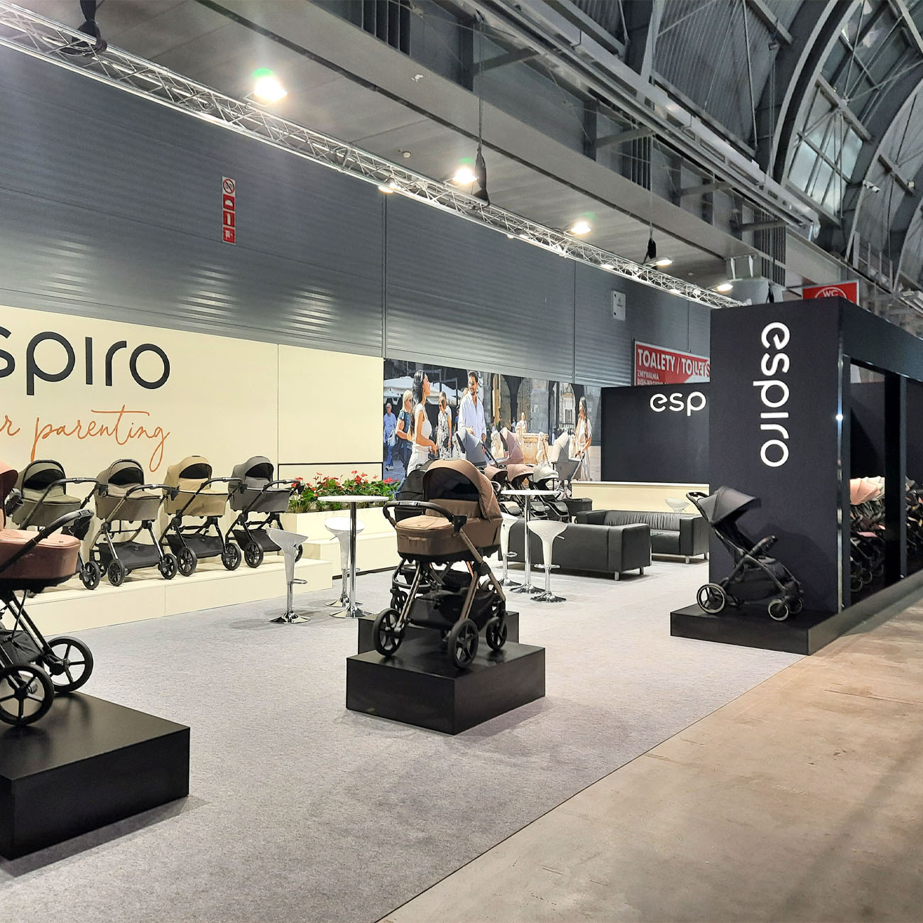 Trade show booth for a solar energy company with two side walls in white and wood tones, featuring solar panels on display and a small meeting area with natural lighting.